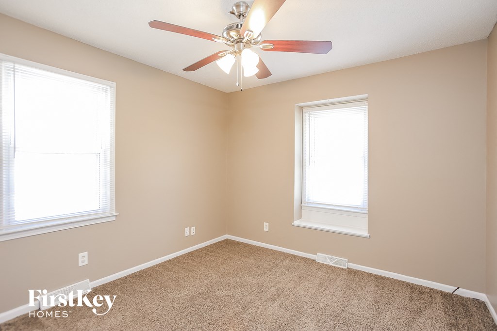 an empty bedroom with a ceiling fan and two windows