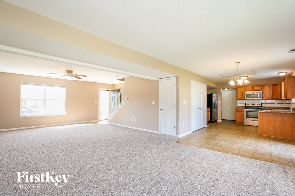 an empty living room with a kitchen and a ceiling fan