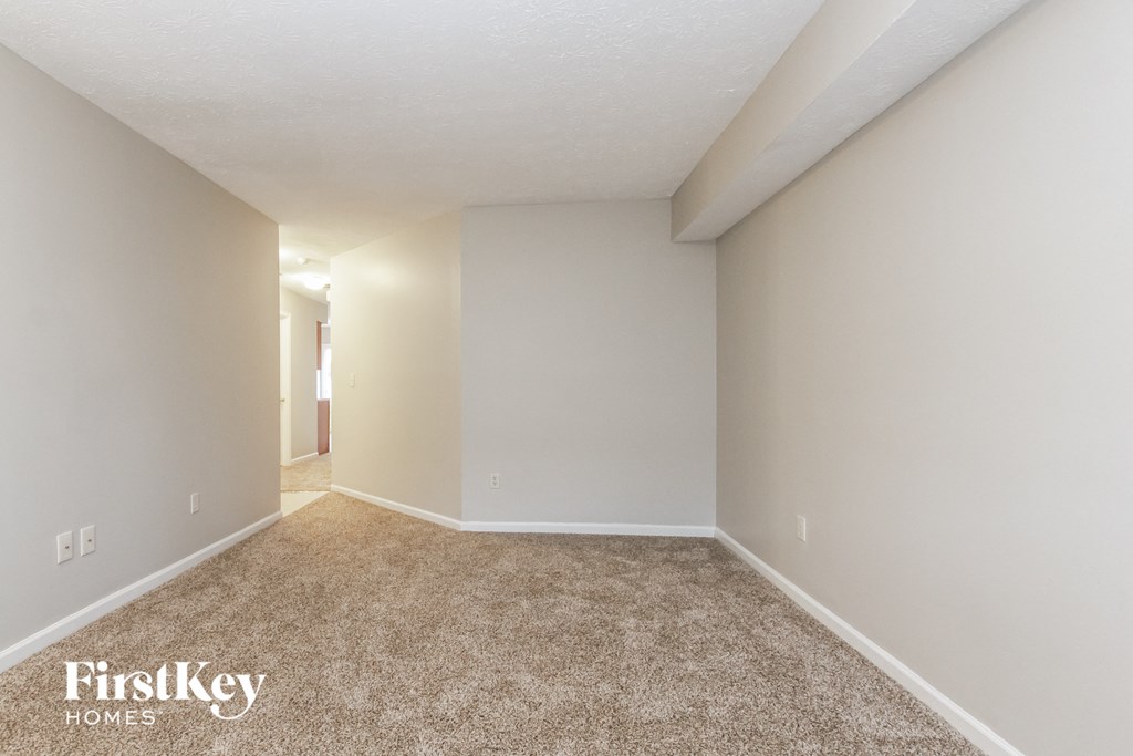 A room with a carpeted floor and white walls, with a doorway leading to another room.