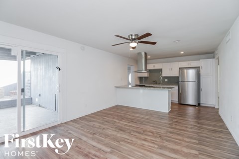 A kitchen with a refrigerator, sink, and stove is shown in a room with wooden floors and white walls.