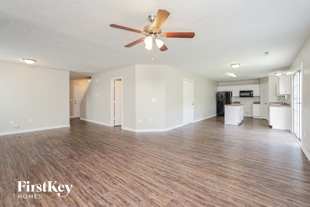 an empty living room with a ceiling fan and a kitchen
