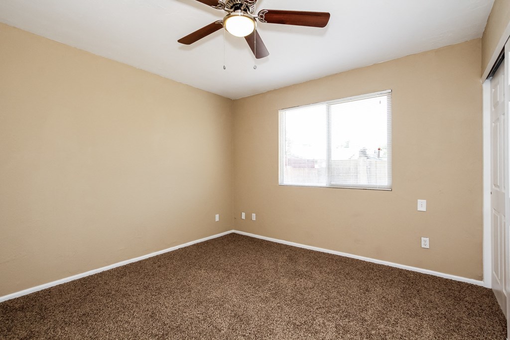 an empty bedroom with a ceiling fan and a window