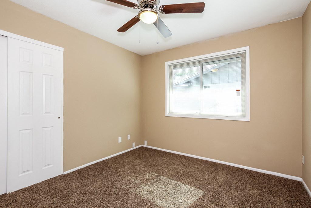 an empty bedroom with a ceiling fan and a window