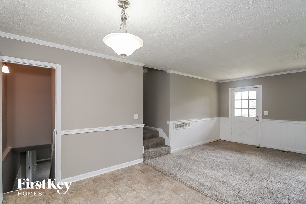 A room with a carpeted floor and a staircase leading to another room.