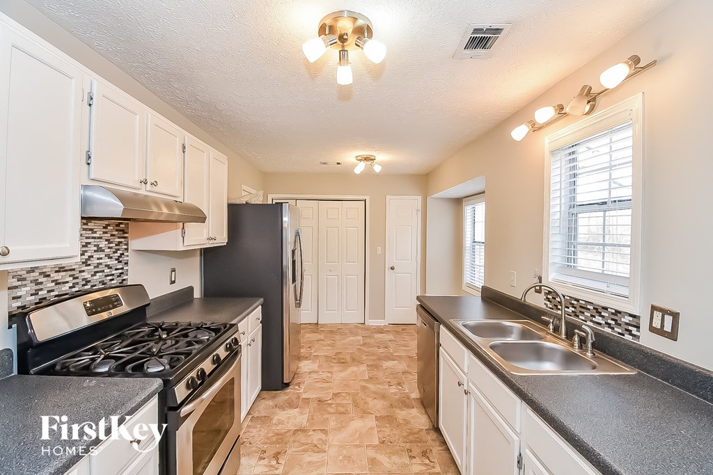a kitchen with white cabinets and black counter tops and a stove and sink