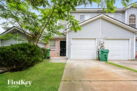 a white house with a white garage door and a green trash can