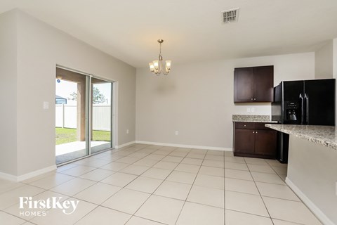 A spacious kitchen with a black fridge and microwave, a white countertop, and a chandelier hanging from the ceiling.