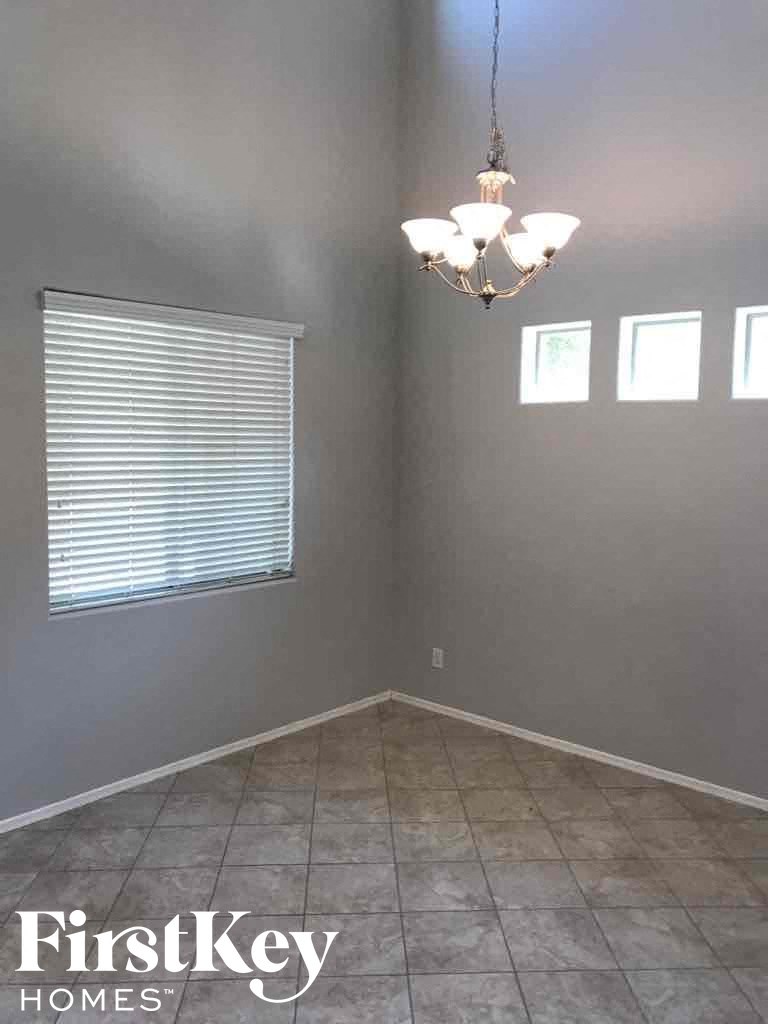 A room with a chandelier, tiled floor, and a window with blinds.