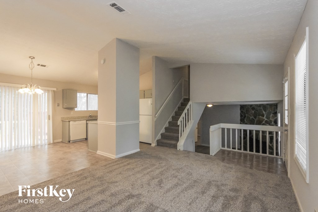 an empty living room with a staircase and a kitchen