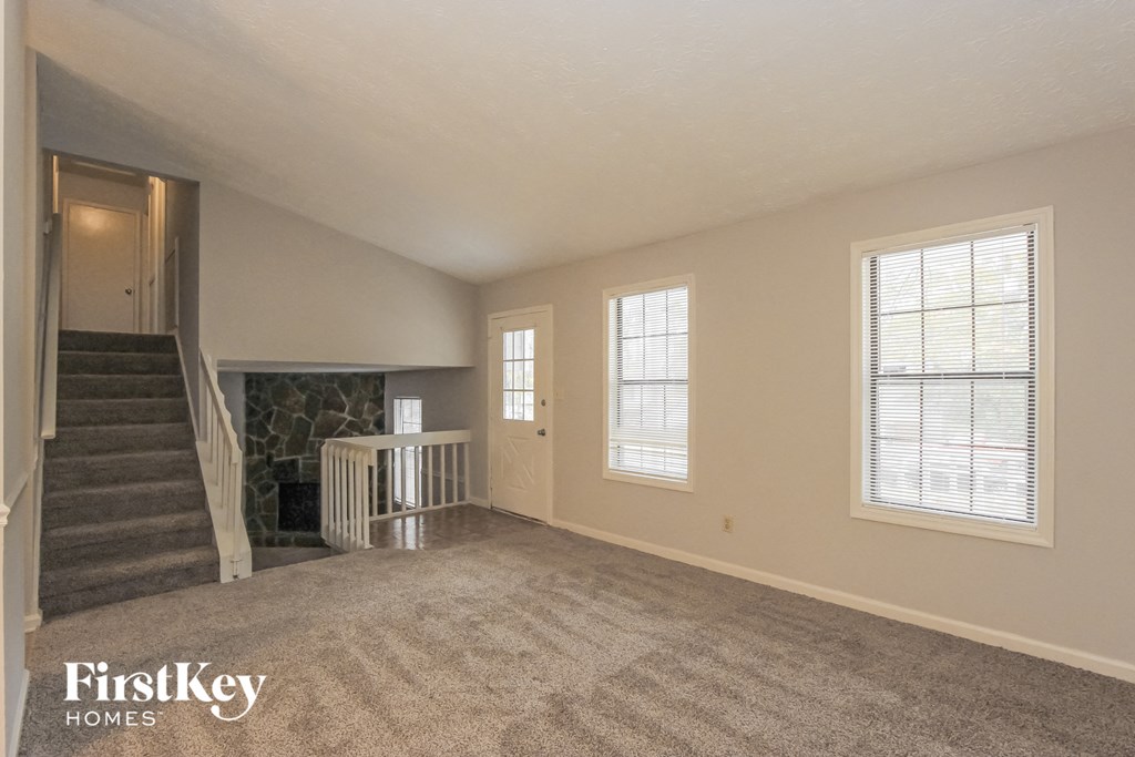 an empty living room with a staircase and a stone fireplace