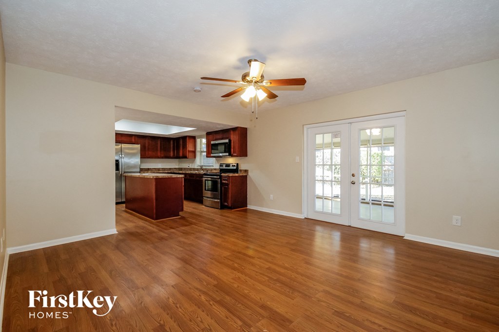 an empty living room with a ceiling fan and a kitchen