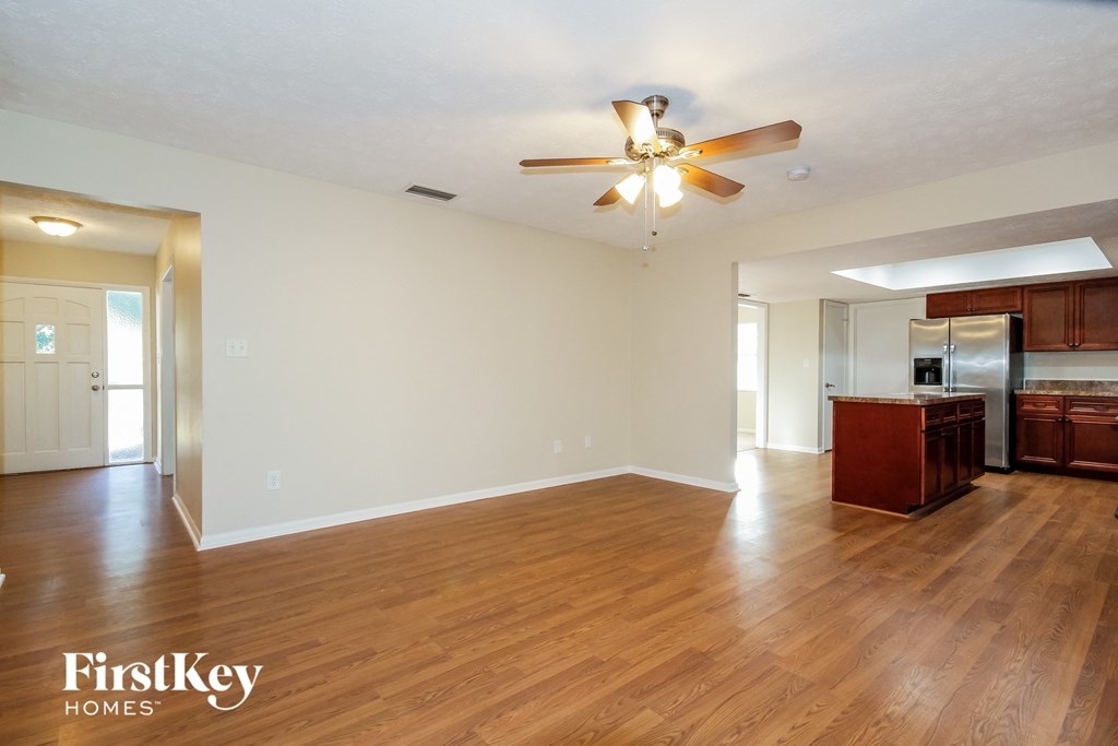 an empty living room with a ceiling fan and a kitchen