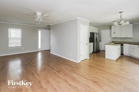 A spacious room with wooden floors and a kitchen area in the background.