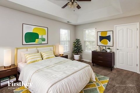 A bedroom with a large bed, a ceiling fan, and two framed artworks on the wall.