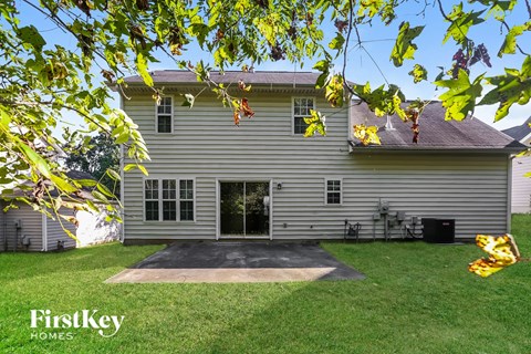 A house with a grey siding and a black door is surrounded by green grass.