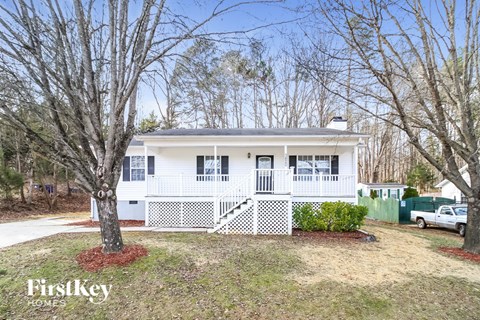 A white house with a porch and a tree in front.