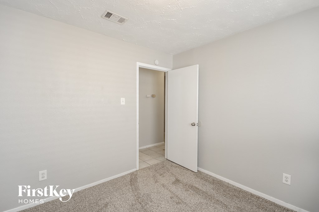 a bedroom with white walls and carpet and a door to a closet