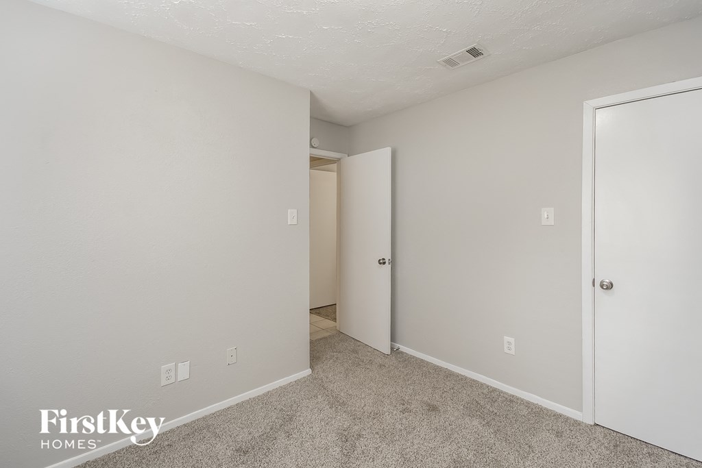 a bedroom with white walls and carpet and a door to a closet
