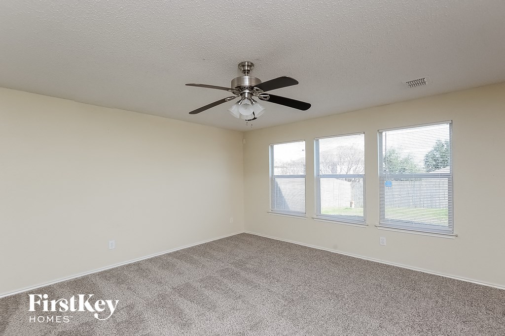 an empty living room with a ceiling fan and three windows
