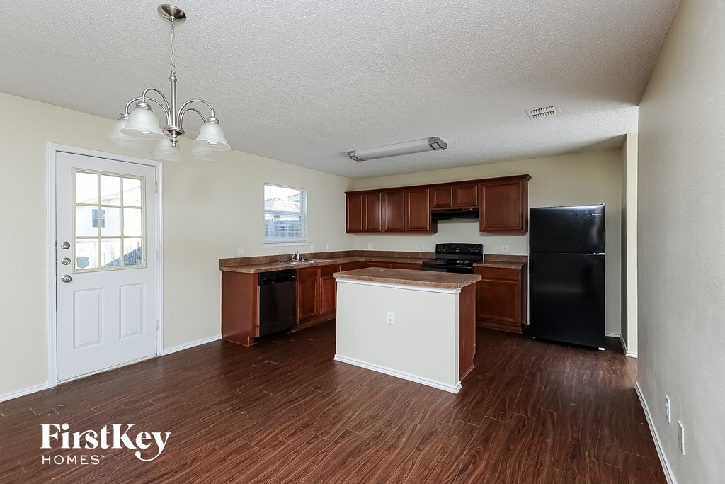 an empty kitchen with wood flooring and a black refrigerator