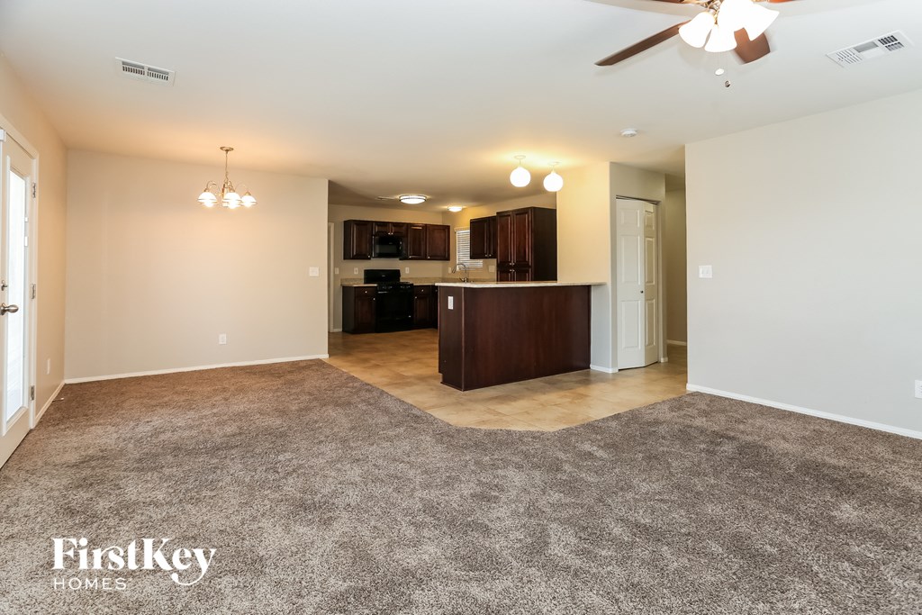 a living room and kitchen with carpeting and a ceiling fan