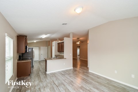 an empty living room and kitchen with wood flooring and white walls