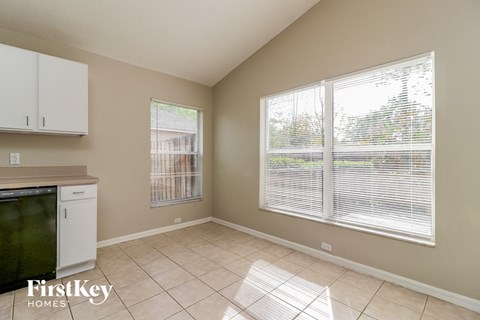 A kitchen area with a refrigerator, cabinets, and a window with blinds.