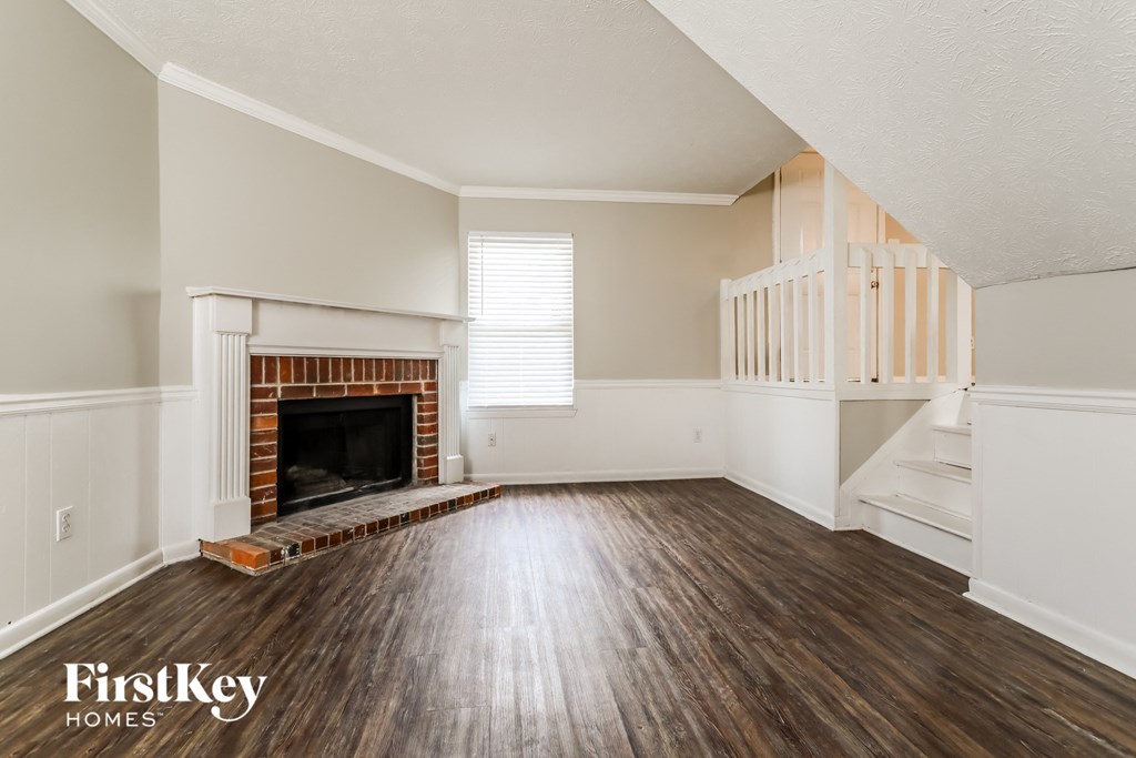 an empty living room with a brick fireplace and wooden floors