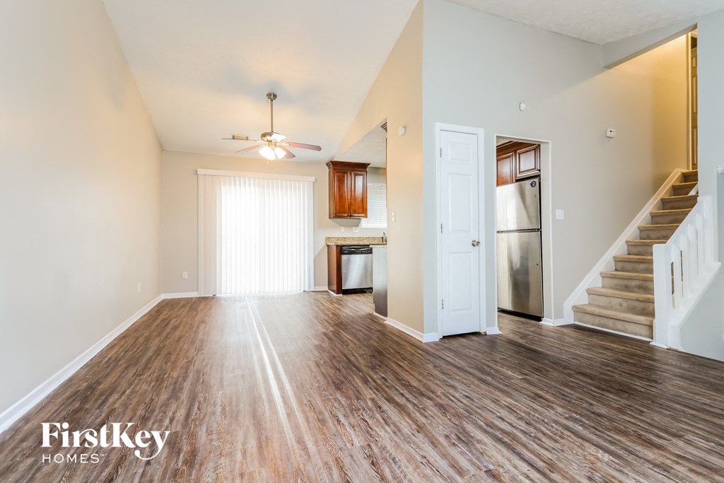 the living room and kitchen of an open floor plan with stairs and a ceiling fan