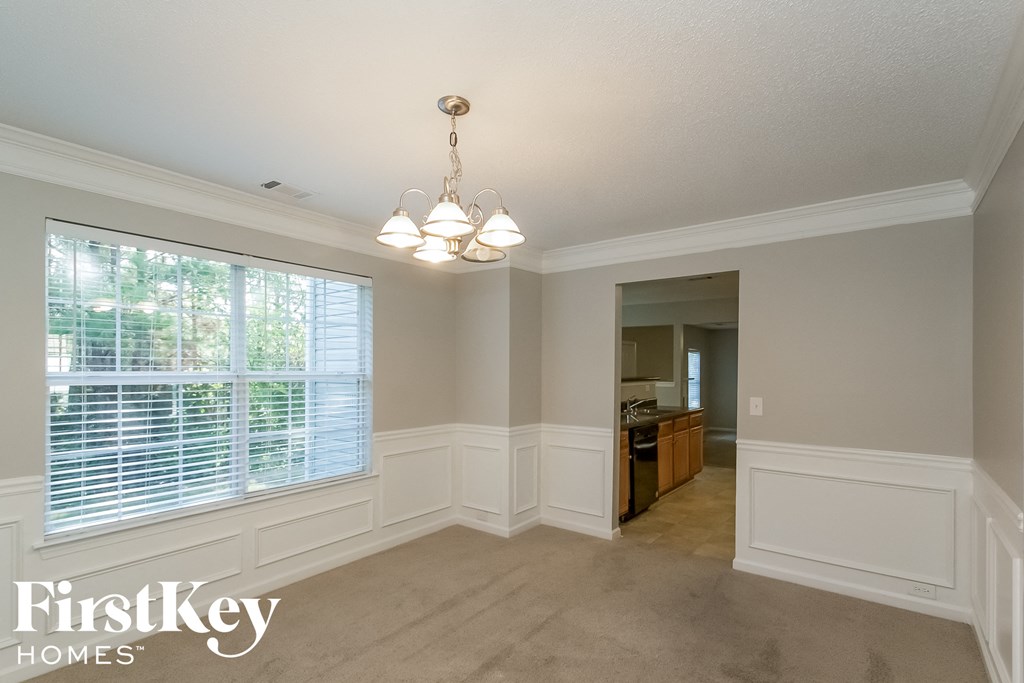 A well-lit, empty room with a chandelier and a window with blinds.