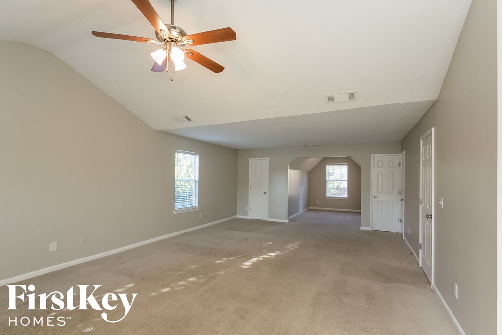 A spacious empty room with a ceiling fan and a window.