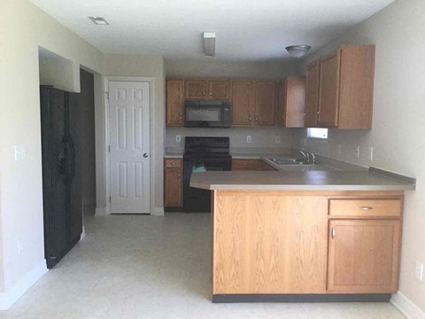A kitchen with wooden cabinets and a black refrigerator.