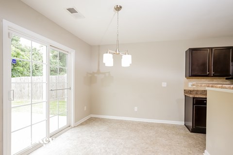A well-lit, empty room with a fireplace and a window with a view of a fence and trees.