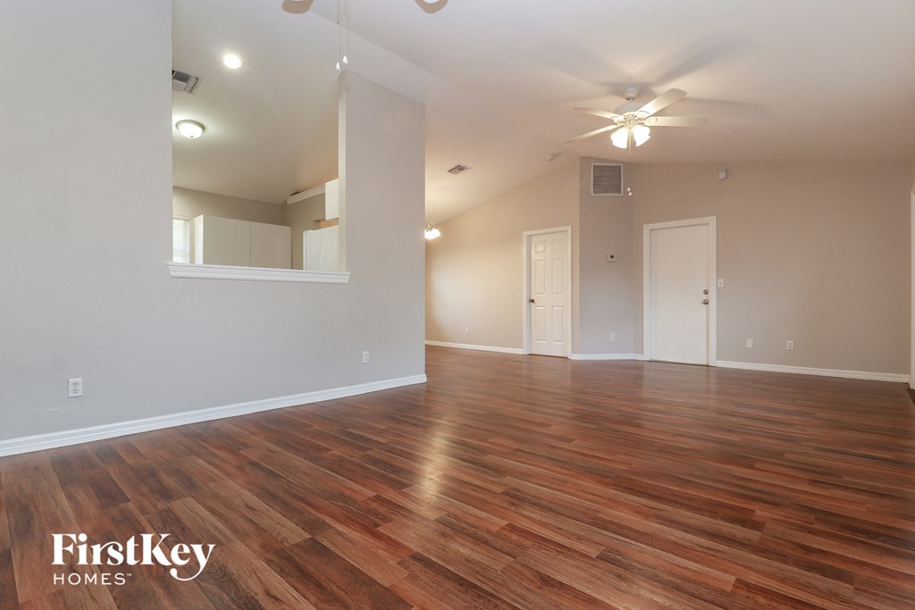 the spacious living room with hardwood flooring and a ceiling fan