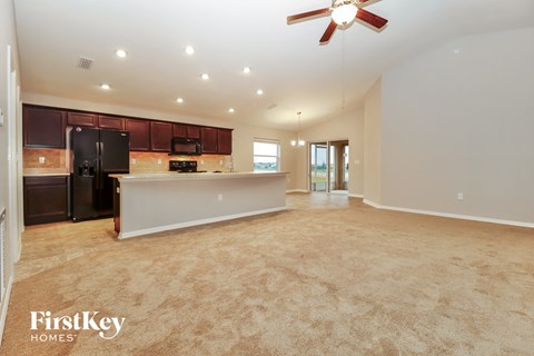 A spacious kitchen and living room with a black refrigerator and a ceiling fan.
