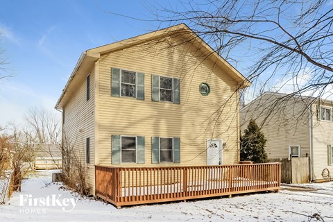 a yellow house with a wooden deck in the snow