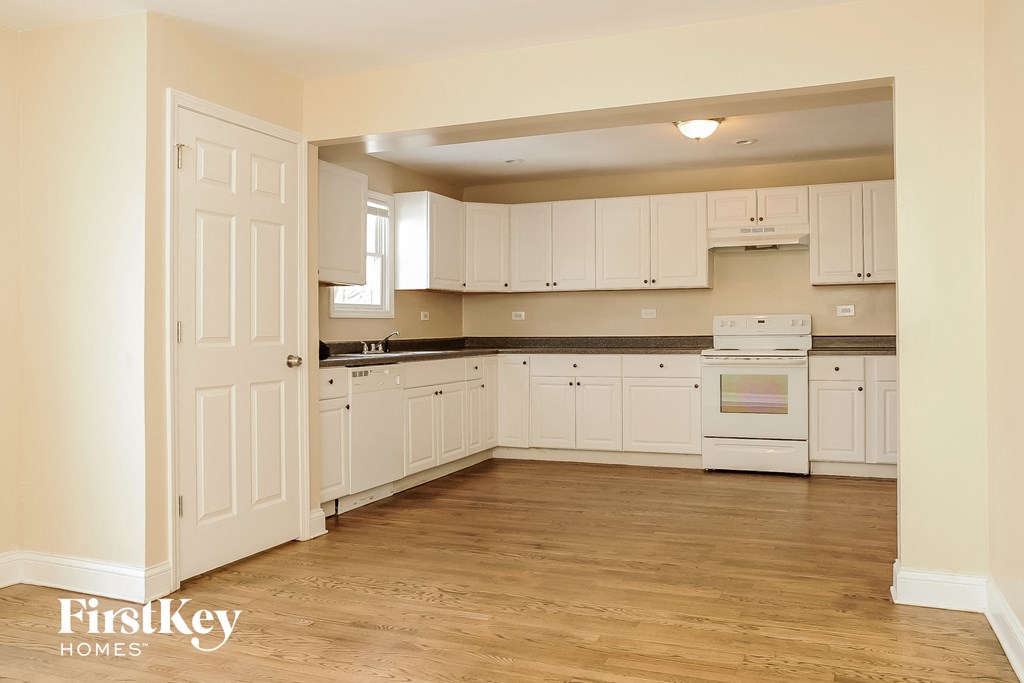an empty kitchen with white cabinets and a wooden floor
