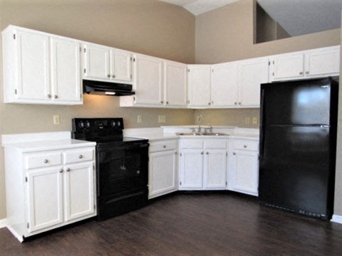 A black refrigerator sits in a kitchen with white cabinets.