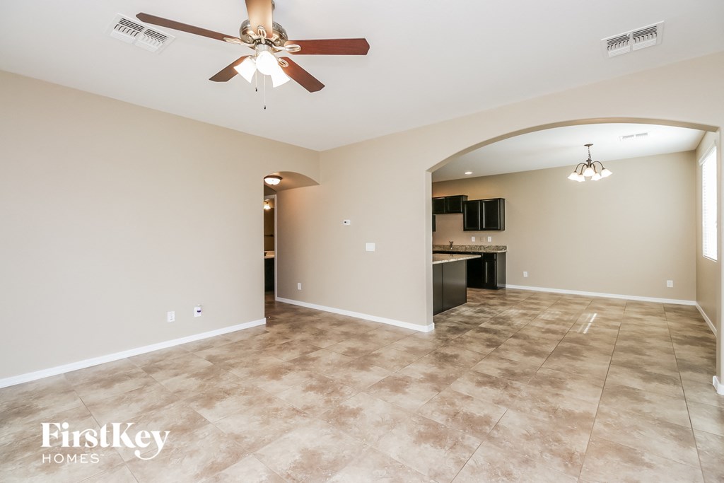 an empty living room with a ceiling fan and a kitchen