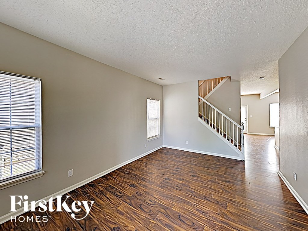 A spacious room with wooden flooring and a staircase in the background.