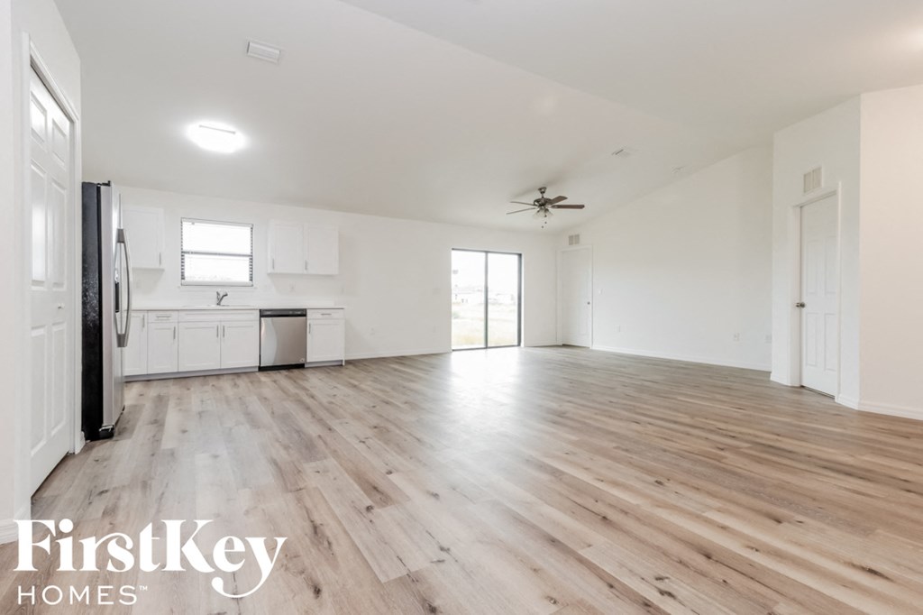 an empty living room and kitchen with wood flooring and white walls