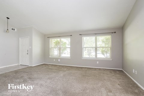 A spacious room with a carpeted floor and two windows.