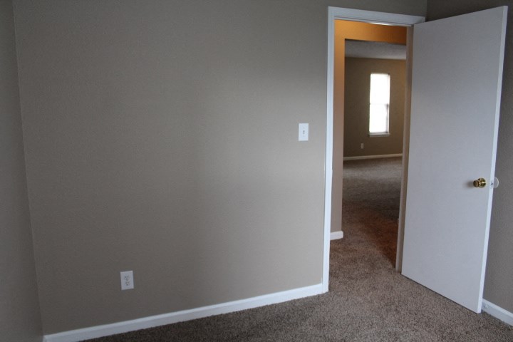 an empty room with a hallway and a door to a bedroom