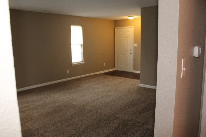 an empty living room with a white door and brown carpet