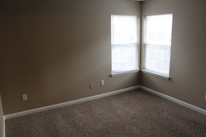 an empty room with two windows and a carpet