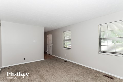 A sparsely furnished room with a carpeted floor and a window with blinds.