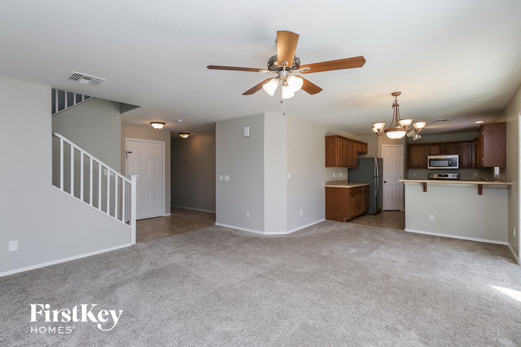 A spacious living room with a ceiling fan and a kitchen area in the background.