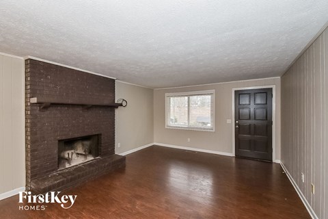 an empty living room with a brick fireplace and wooden floors