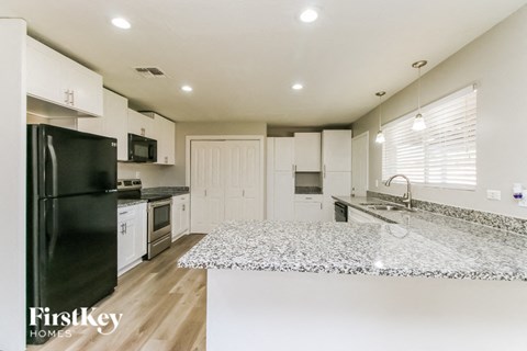 A kitchen with a black fridge, white cabinets, and a granite countertop.