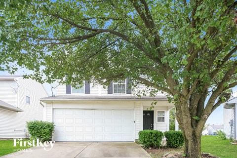 A tree in front of a white house with a garage door.